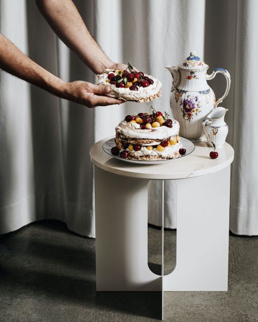 Man's arms are holding a fruit cake in front of small table with more cake and tea tableware
